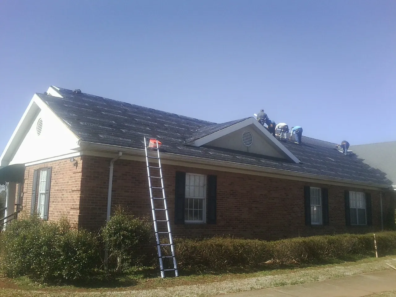 Crew tearing shingles off a brick ranch roof with a ladder set — Metal Roof Repair work by our crew in Washington Depot