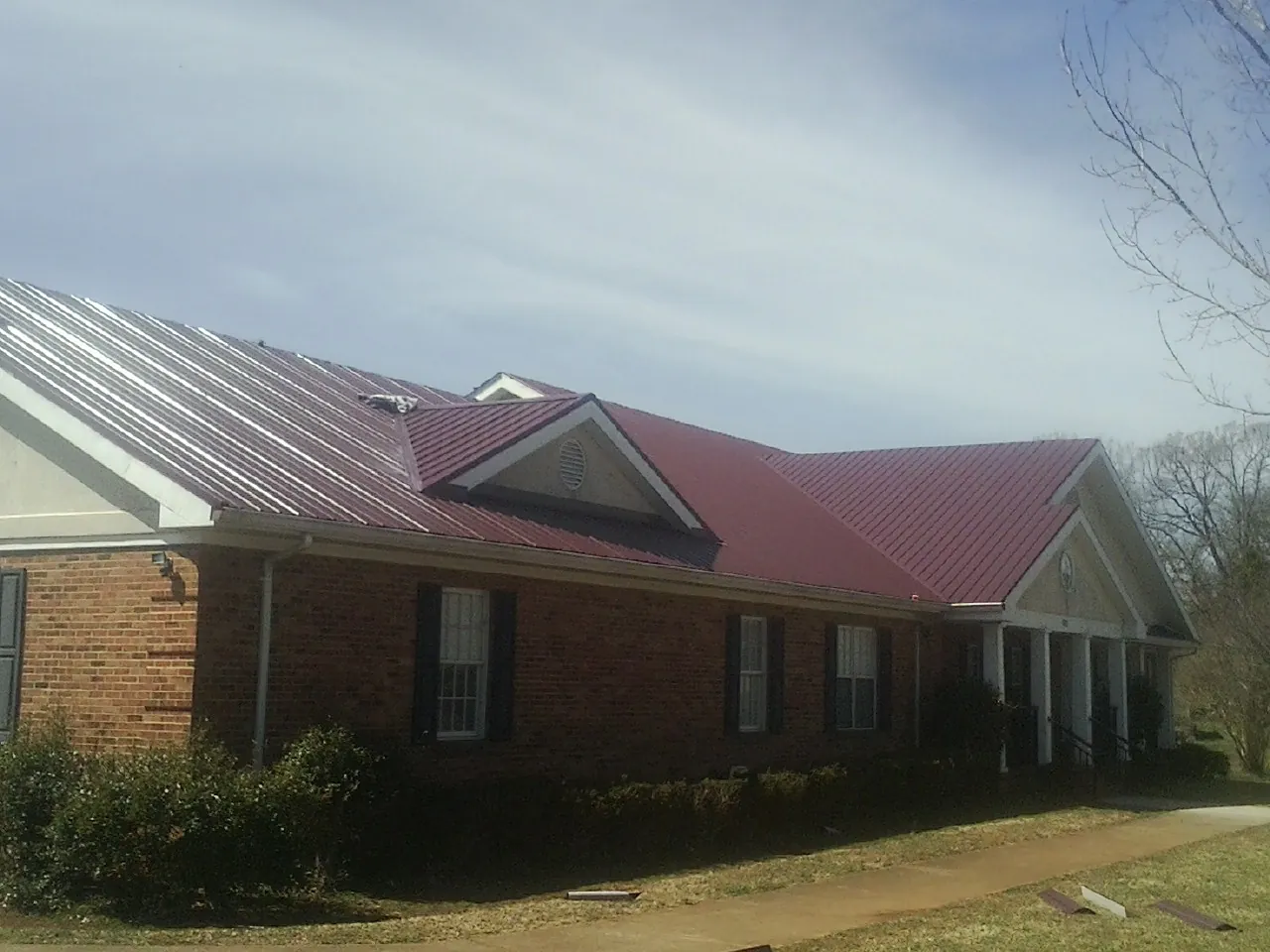 Red metal roof with gabled entries on a long brick building, from a Hail Damage Roof Repair job in Washington Depot