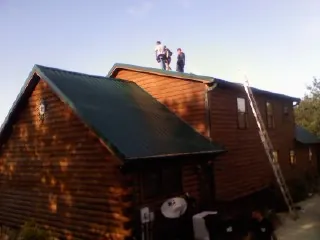 Crew on the ridge of a green metal roof on a two story log home in Washington Depot