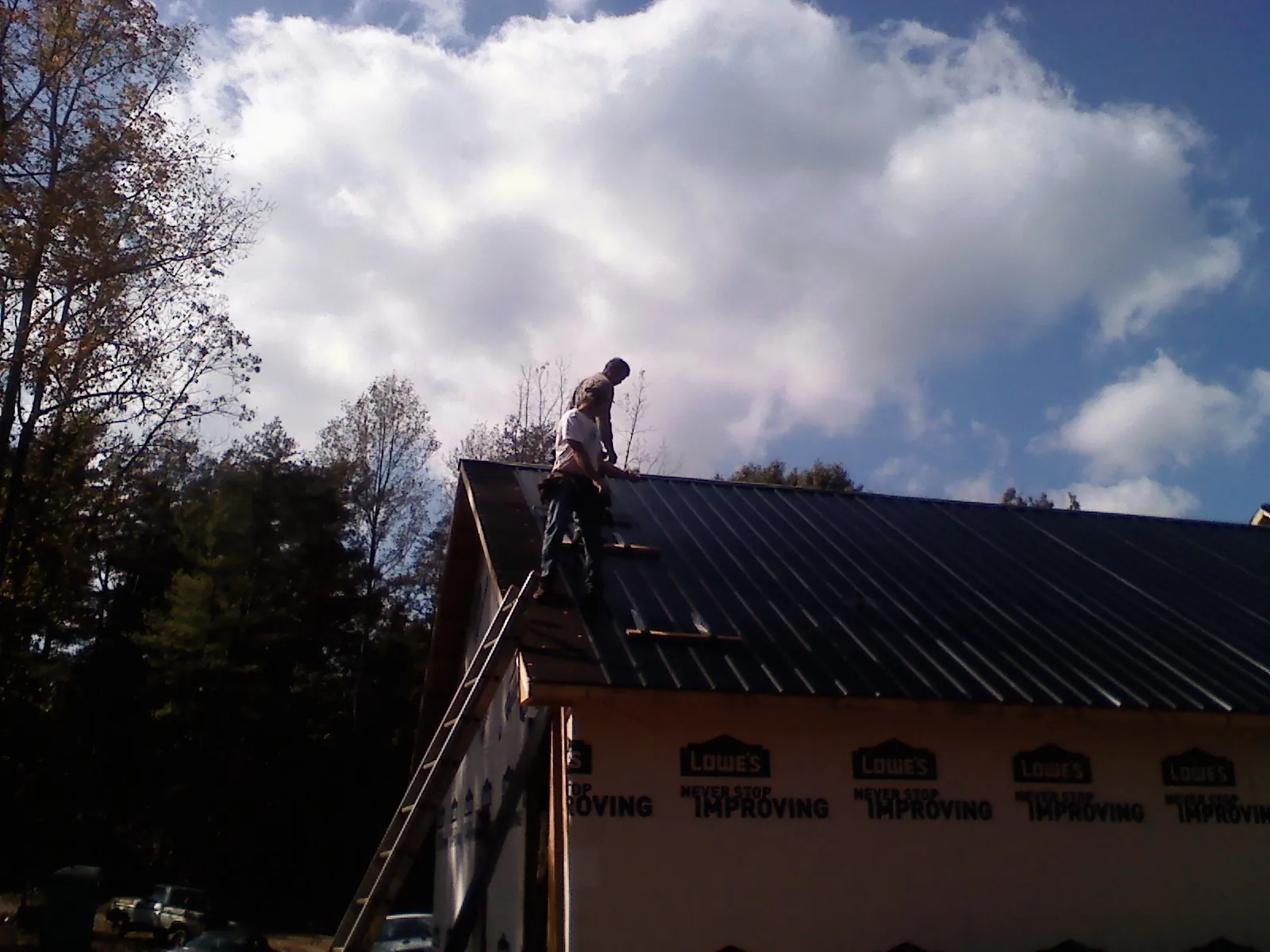 Roofer fastening dark metal panels high against a cloudy sky, from a Roof Inspection job in Washington Depot