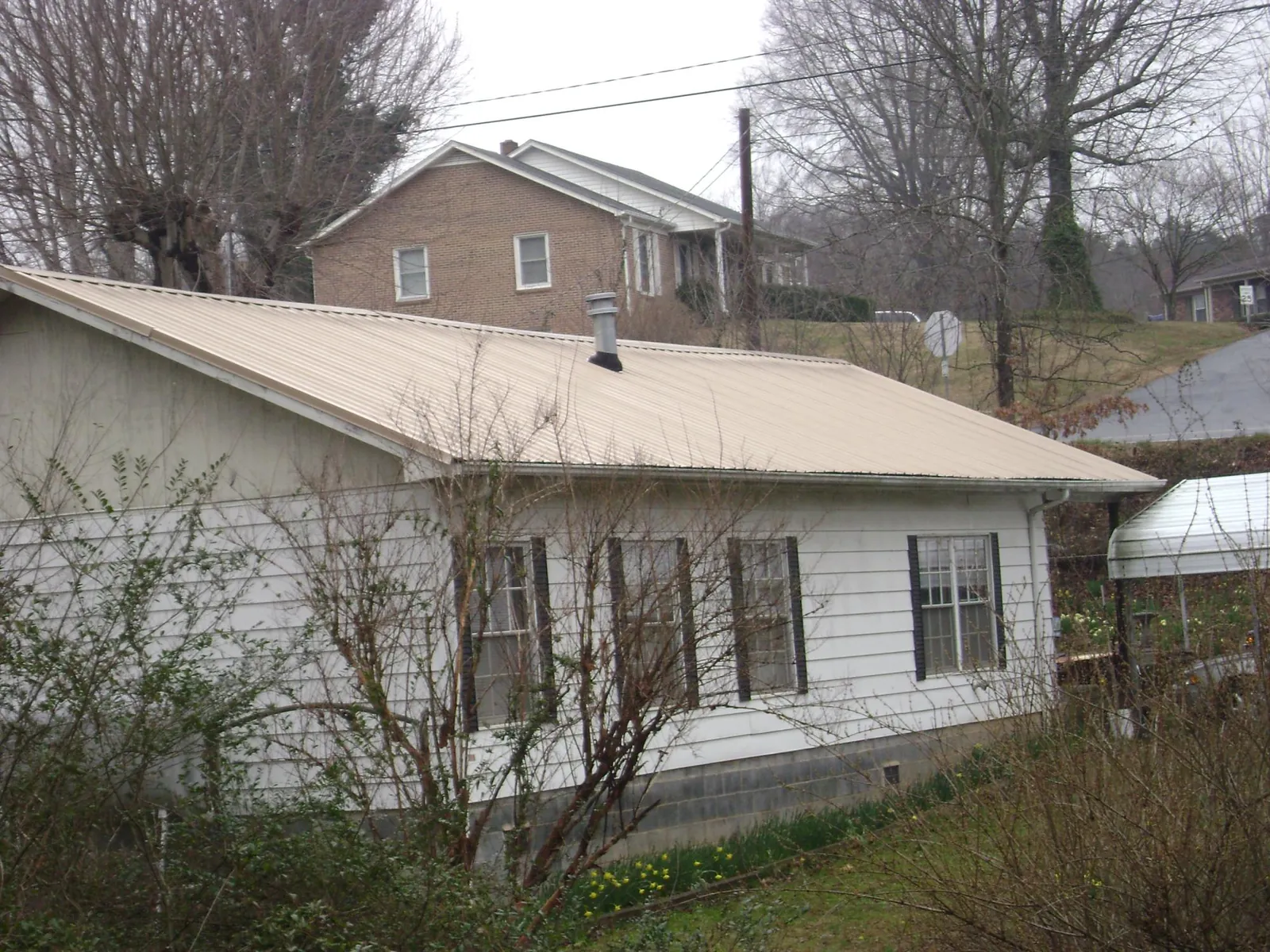 Tan metal roof on a white sided house set into a hillside — Commercial Roofing by Roofing Brothers in Washington Depot